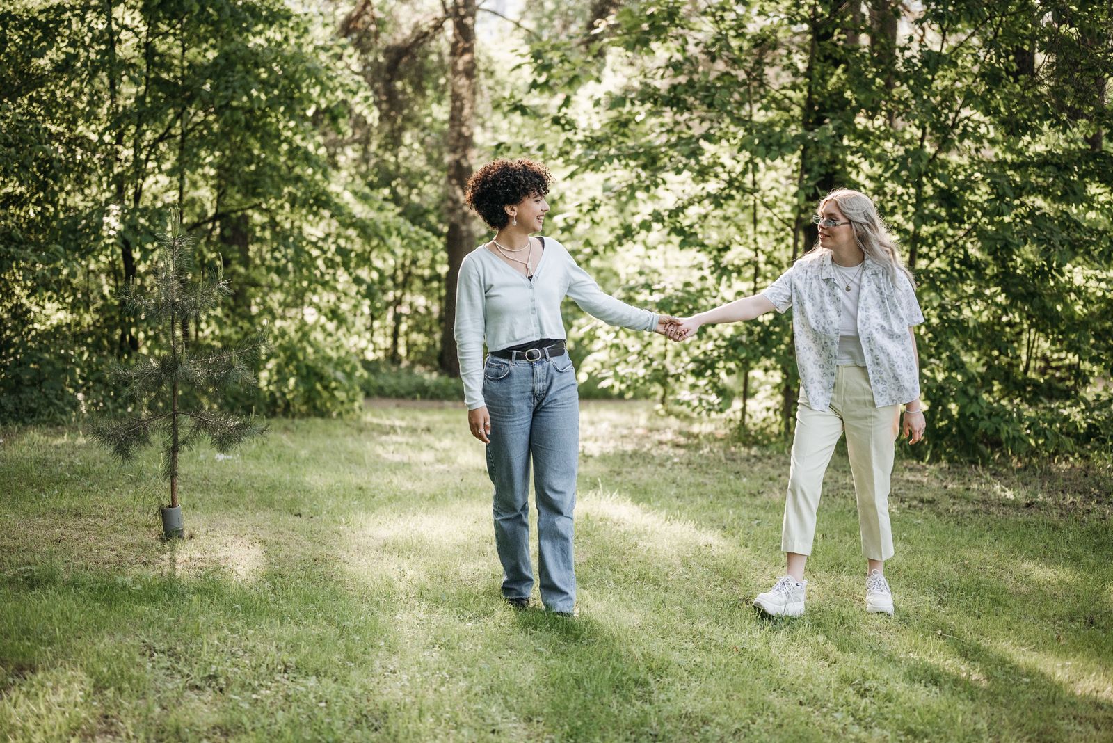 Two women holding hands walking through a sunny park